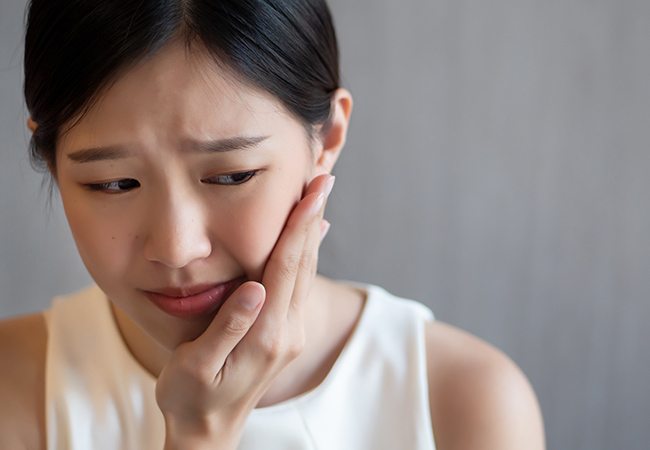 歯の痛みで頬に手をあてる女性
